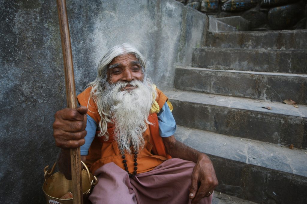 Portrait of an elderly man with a long beard sitting on outdoor stone steps.