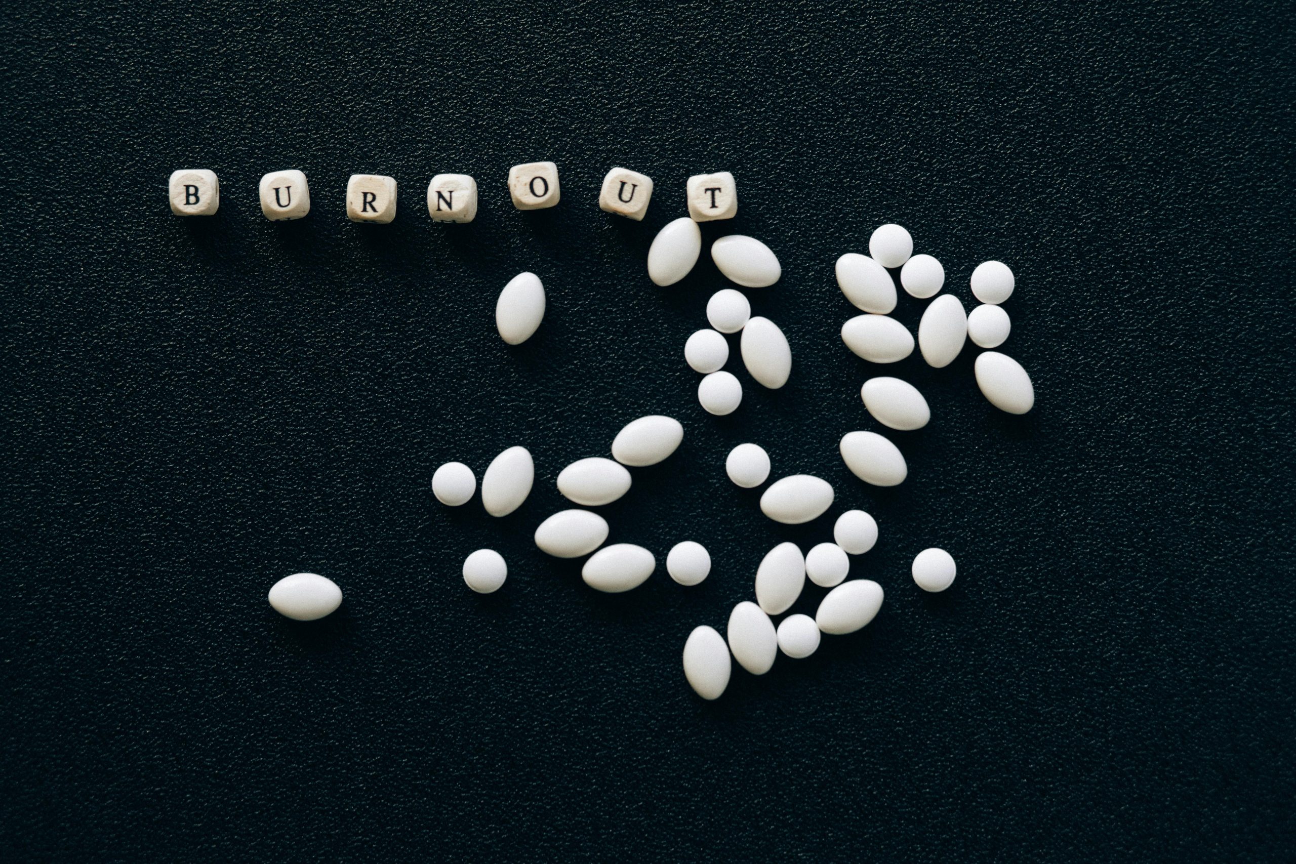 White pills arranged on a black surface spelling 'burnout', symbolizing stress and fatigue.