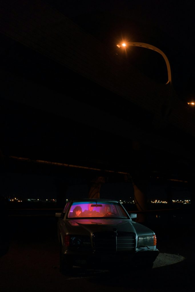 Car parked at night with street lights and cityscape, moody ambiance.