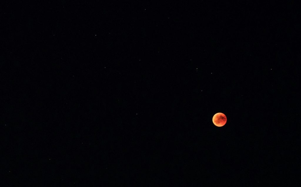 Blood moon eclipse visible over a starry sky in Mönchberg, Germany. Cosmic phenomena captured at night.