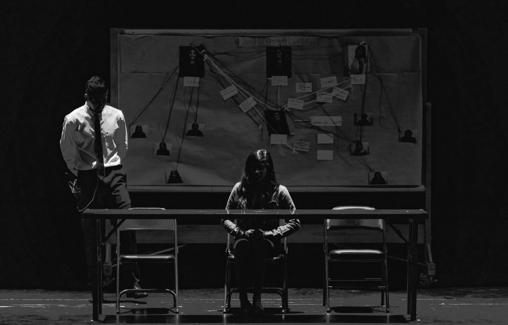 Black and white scene depicting a tense interrogation with suspect and investigator.