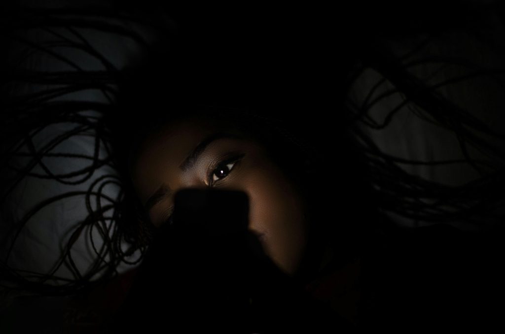 Close-up of a young woman using a smartphone in a dimly lit room, her face illuminated by screen light.