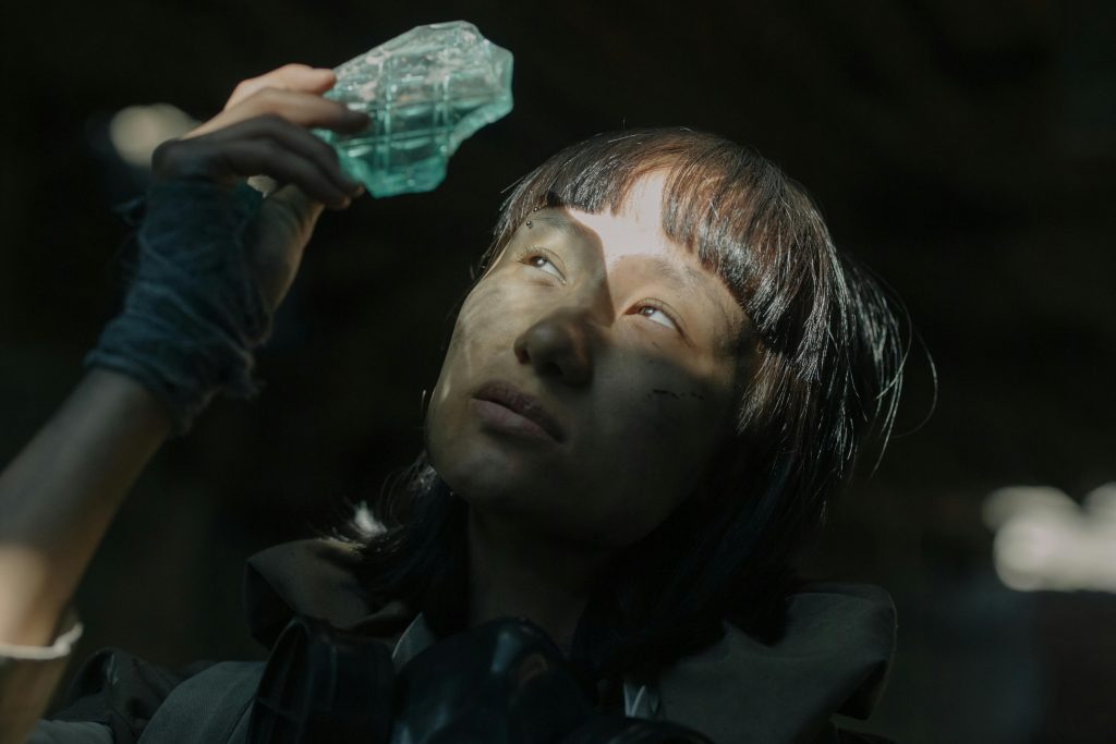 A woman holding a glass shard, immersed in thought in a post-apocalyptic setting.