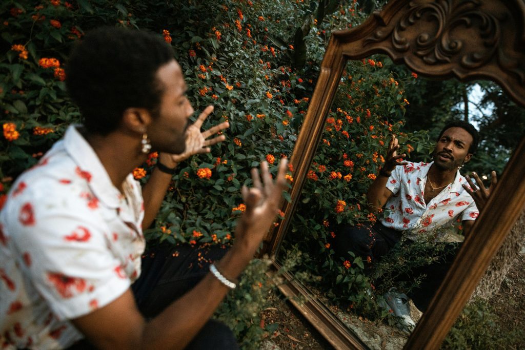 Man expressing in front of a mirror with vibrant flowers outdoors. Reflective mood.