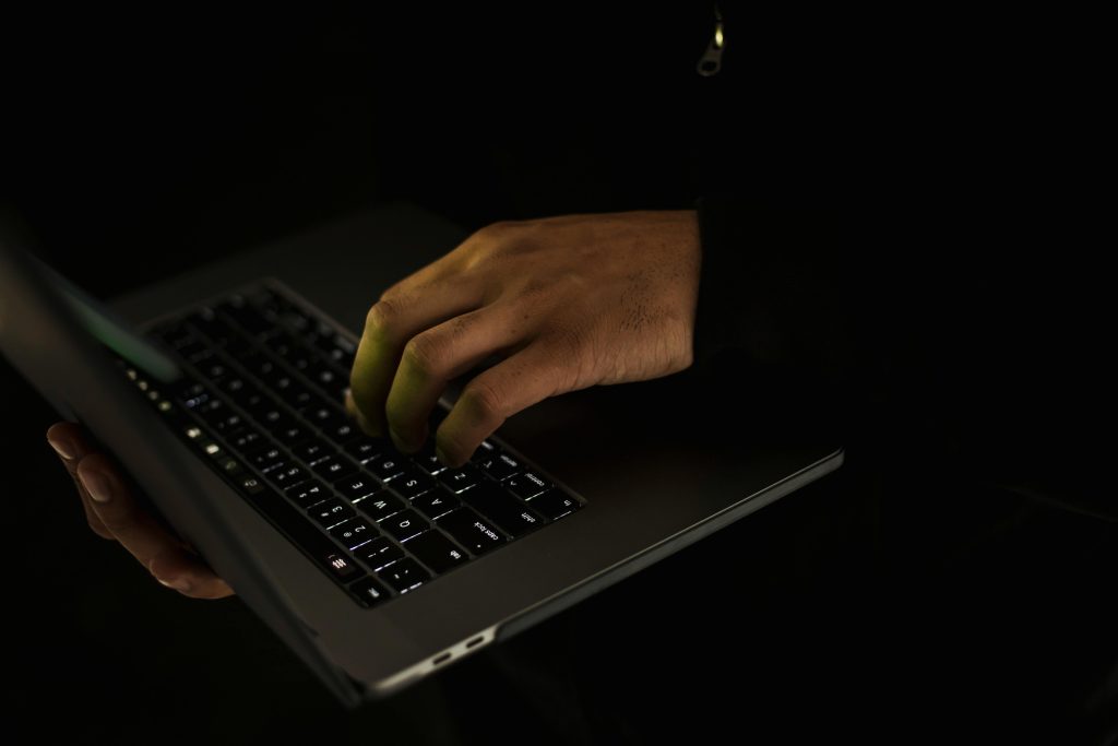 Crop unrecognizable male in black sweater holding netbook on hand and typing on keypad in dark room