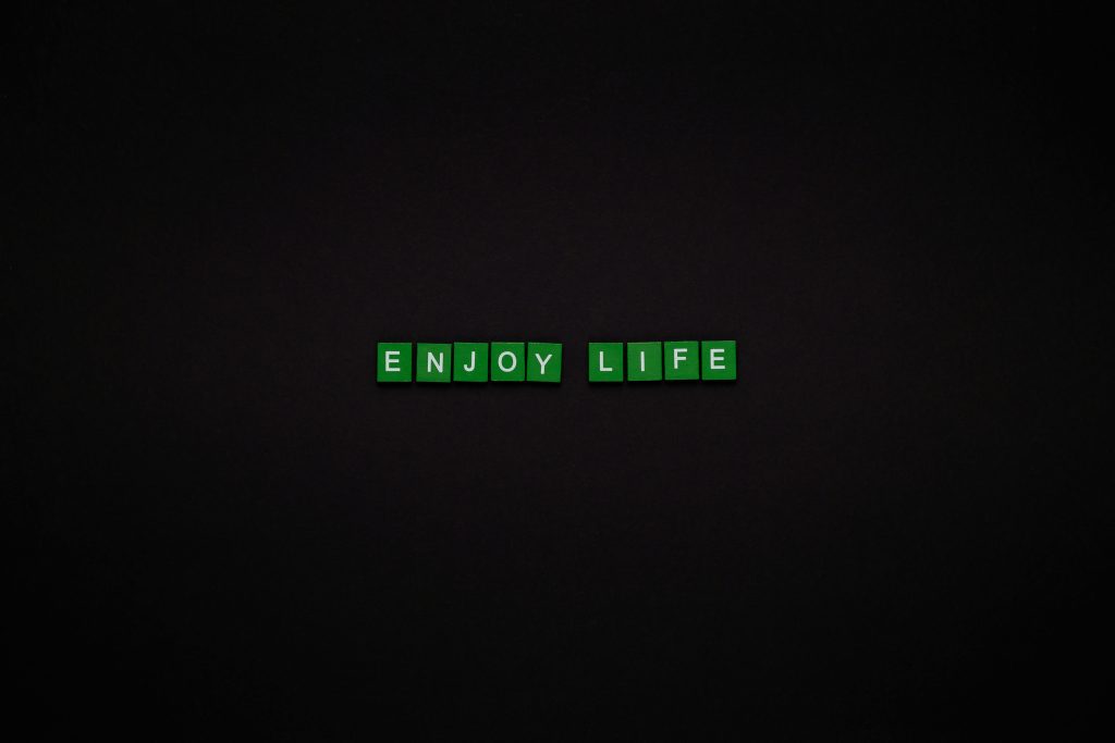 Green letter tiles spelling 'ENJOY LIFE' on a black background, perfect for motivational content.