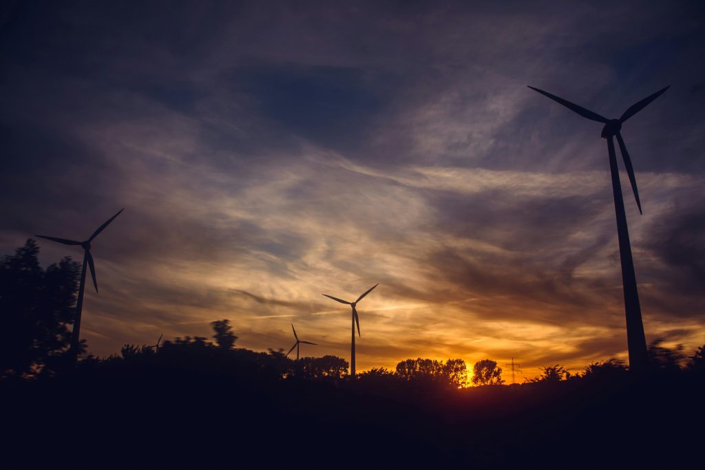 Silhouetted wind turbines at sunset, showcasing renewable energy against a vibrant sky.