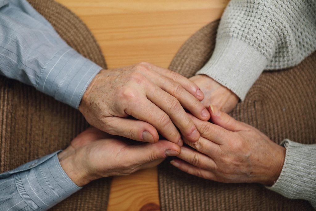 Close-up of elderly hands holding on a wooden table, symbolizing love and connection.