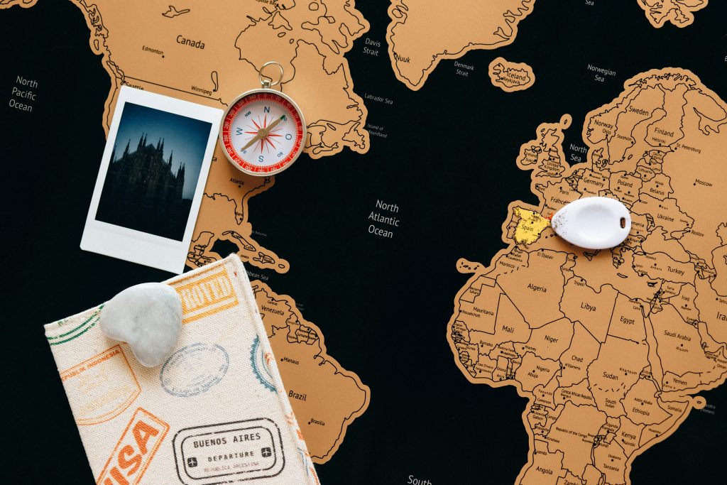 Flat lay of travel items including a map, compass, and polaroid for adventure planning.