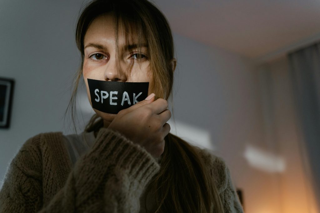 A woman with 'SPEAK' taped over her mouth, symbolizing silence and oppression.